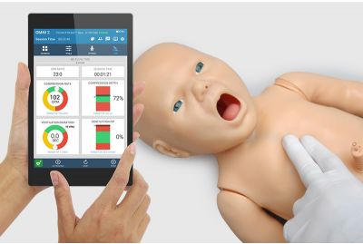 A learner performs two-finger compressions on the Newborn PEDI skills trainer; the handheld OMNI2 displays CPR quality.