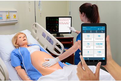 A learner feels the belly of a NOELLE simulator and reads a virtual monitor; a handheld OMNI2 controller changes the FHR