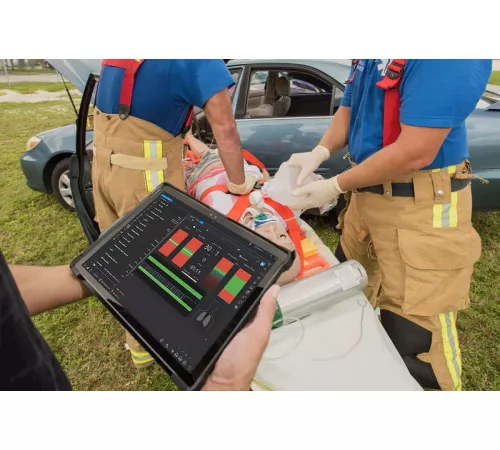 Trauma HAL patient simulator strapped to stretcher next to vehicle collision while two paramedics perform an assessment